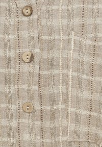 Beige button-down skjorte med struktureret stof og lodrette striber, træknapper og en lomme detalje.