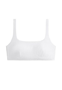 Crop top blanc avec larges bretelles et motif floral discret en œillets, posé à plat sur fond blanc.