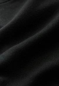 Schwarzer Stoff mit glatter Textur, der subtile Falten und ein mattes Finish aufweist. Keine Muster oder sichtbaren Beschläge.