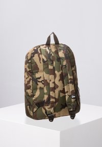 Mochila de camuflaje con un diseño acolchado, material de tela, detalles en marrón, correas ajustables dobles y un bolsillo de malla en el lateral.