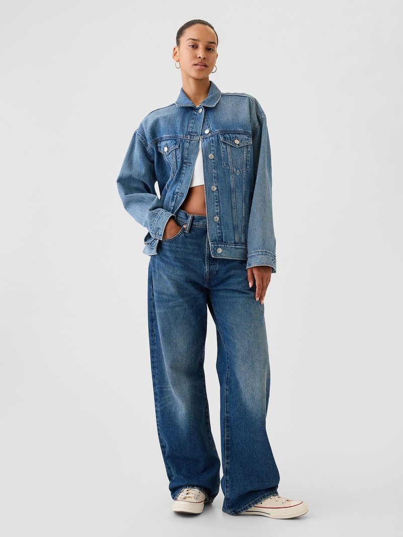 Jeansjacke mit klassischem Schnitt, hellblauem Waschung und frontalen Taschen, kombiniert mit weit geschnittenen blauen Jeans und weißen Sneakers.
