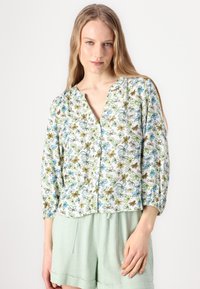Loose-fitting, button-front blouse in white with a floral pattern featuring blue, green, and brown flowers. Long sleeves with elastic cuffs.