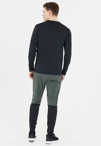 Långärmad svart träningsskjorta med rund halsringning, i kombination med gröna och svarta smala byxor. Bekvämt tyg med en mjuk textur.