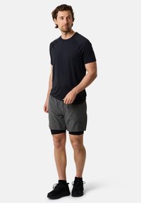 Zwart sportshirt met korte mouwen gecombineerd met grijze shorts. Schoenen zijn zwart met een gestructureerd oppervlak. Eenvoudig, functioneel ontwerp.