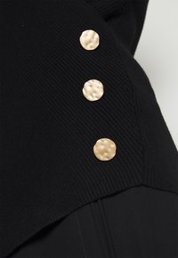 Gros plan sur un tissu côtelé noir avec trois boutons circulaires dorés texturés disposés verticalement.