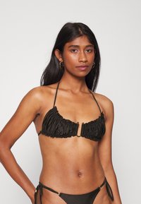 Top de biquíni preto com textura franzida e detalhes em tom dourado. O pescoço halter e as laterais com laços oferecem ajuste e suporte ajustáveis.