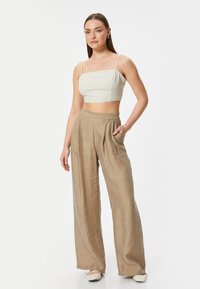 Crop top i lysegrøn og hvid ternet mønster, parret med højtaljede, brede beige bukser med plissee; minimalistisch design.
