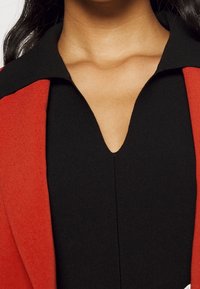 Czarna bluzka z głębokim dekoltem w serek, wyposażona w otwarty kołnierz z czerwonej tkaniny, wyróżniająca się gładką fakturą i dopasowanym krojem.