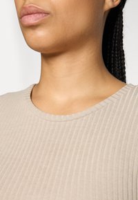 Haut beige à côtes avec un col rond, texture lisse et coupe près du corps, mettant en valeur de fines rayures verticales.