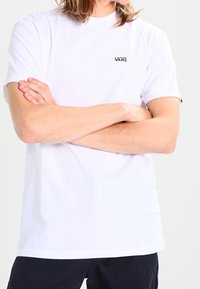 T-shirt blanc à manches courtes en coton avec un col rond et un logo "VANS" noir sur la poitrine gauche. Texture lisse, coupe décontractée.