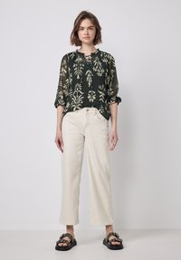 Fließende schwarze Bluse mit floralem Druck, kombiniert mit cremefarbenen, weit geschnittenen Hosen und schwarzen Sandalen mit dekorativen Beschlägen.