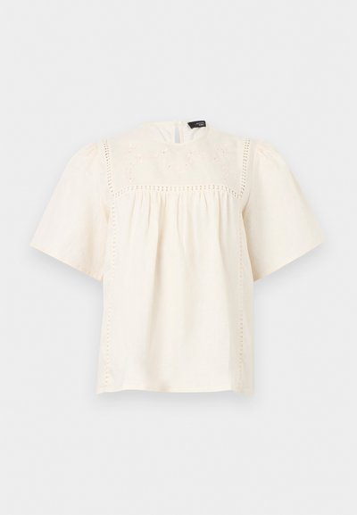 Μπλούζα κοντομάνικη σε κρεμ απόχρωση με ψηλό λαιμό, κεντήματα με τρύπες στο πάνω μέρος του στήθους και στους ώμους, και ελεύθερο, ραμφωτό ύφασμα κάτω από το γιλέκο.