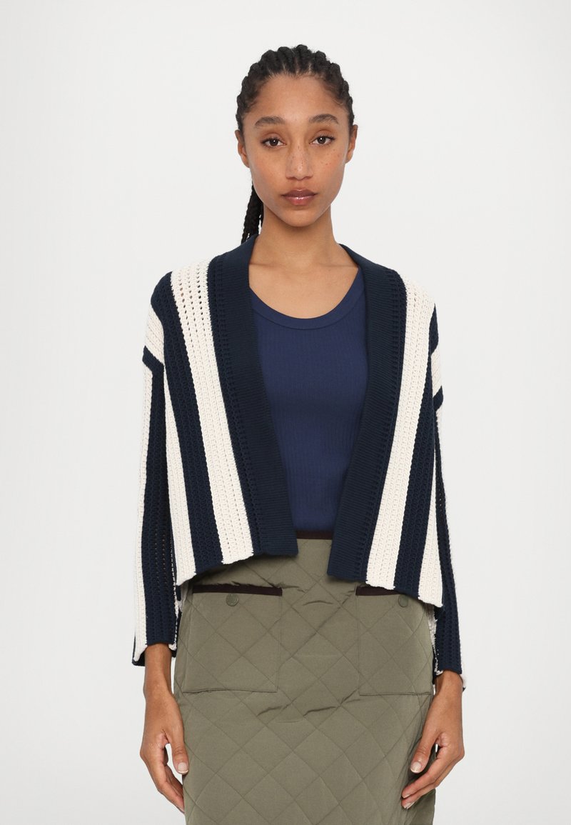 Cárdigan de punto a rayas que presenta colores navy y crema, con apertura frontal, mangas 3/4 y un diseño de tela texturizada. Llevado sobre una blusa navy.