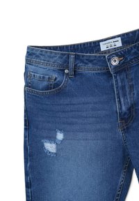 Jeans in denim blu con un design usurato. Le caratteristiche includono una chiusura a bottone, tasche frontali e aree sfilacciate sul tessuto.