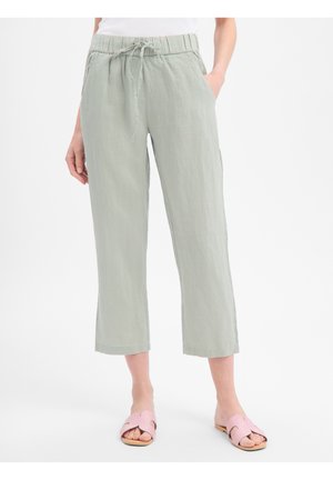 Jasnoszare krótkie spodnie z elastycznym paskiem i sznurkiem, noszone z jasnoróżowymi sandałami typu slide na białym tle.