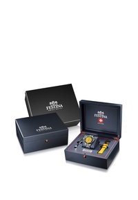 Sort urkasse med røde accenter. Indeholder et ur med gul urskive og et ekstra gult rem. Inkluderer en mærket pen.