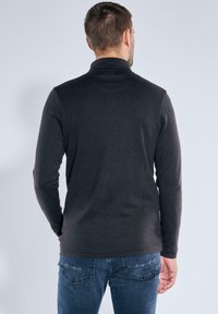 Dunkelgraues, langärmliges Turtleneck-Shirt mit glattem Material; getragen mit blauen Jeans, zeigt die Rückansicht und minimale Designelemente.