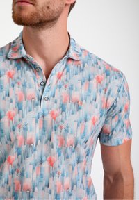 Polo de manga corta en azul claro con un patrón tropical que presenta palmeras rosas y verdes, botones y un pequeño logo en el pecho.