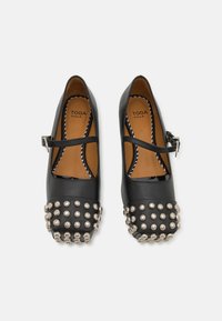 Zapatos Mary Jane de cuero negro con una correa, que presentan una punta redondeada adornada con tachuelas plateadas y una plantilla texturizada en tono marrón.