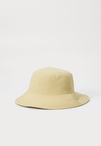 Bøttehatt i lys gul stoff, med en bred, myk søm og syede detaljer langs kanten. Enkel, udekorerte design.