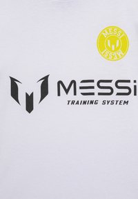 Hvit t-skjorte med svart tekst og logo "MESSI TRAINING SYSTEM", samt en gul sirkelakcent over teksten. Laget av bomull, med rund halsdesign.