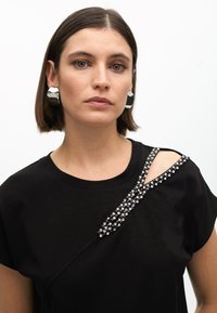 Black short-sleeve top featuring a diagonal line of rhinestones on the shoulder, with an open cutout and soft texture.