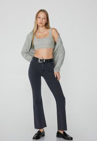 Grauer bauchfreier Top mit Pailletten, kombiniert mit dunkelblauen Schlagjeans und schwarzen Mokassins. Die Jeans haben einen rohen Saumabschluss und einen schwarzen Gürtel.