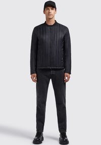 Black padded bomber jacket with vertical quilted lines, zip closure, ribbed collar, worn with black jeans and chunky black boots.