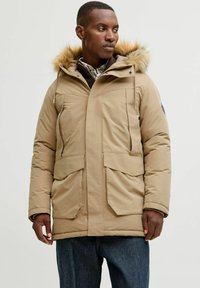 Parka beige isolato con cappuccio foderato in pelliccia, dotata di due ampie tasche frontali e chiusura con zip, realizzata in tessuto liscio e resistente all'acqua.