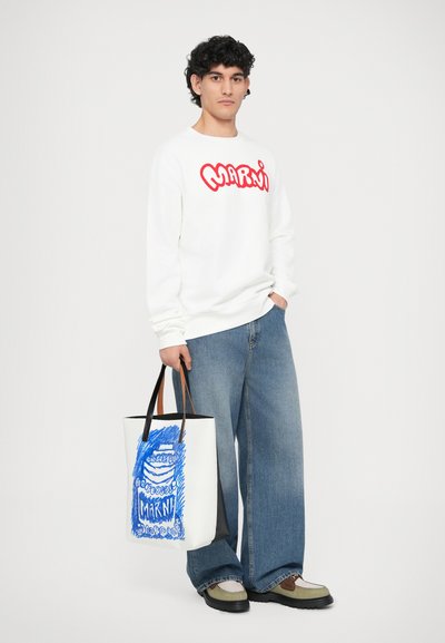 Sudadera blanca con el logo rojo de "Marni", combinada con unos vaqueros de pierna ancha azules y una bolsa de mano gráfica con arte azul y acentos negros.