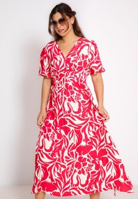 Floral maxi-jurk in felrood en crèmekleur. Korte mouwen, V-hals, een gecinchte taille en een vloeiende rok met bladeren- en bloemenpatronen.