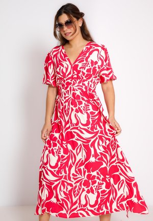 Robe maxi florale en rouge vif et crème. Manches courtes, décolleté en V, taille cintrée et jupe fluide avec des motifs de feuilles et de fleurs.