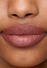 Matte lipkleur in een gedempte mauve tint, met een soepele textuur en fijne lijntjes. Focus op de vorm en volheid van de lippen.