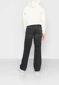 Jeans de mezclilla negra con un corte recto, bolsillos traseros y detalles de costura sutiles, combinados con una sudadera de color claro y zapatillas deportivas.