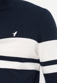 Pull bleu marine avec des rayures horizontales blanches sur la poitrine et les manches, avec un petit logo d'oiseau blanc brodé sur la poitrine.