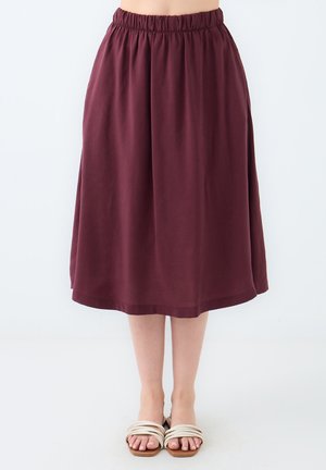 Jupe bordeaux, longueur genou, en tissu souple avec un waistband élastique et un design fluide. Associée à des sandales à lanières de couleur claire.