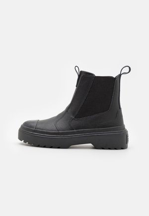 Black leather Chelsea boot with elastic side panels, thick sole, and pull tabs at front and back, shown in side profile on white background.