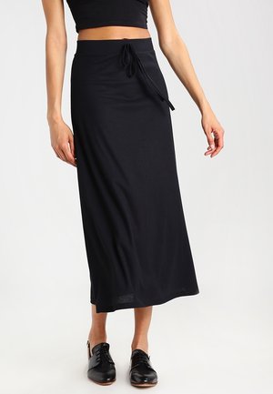 Jupe maxi noire à côtes avec taille à cordon. Le tissu est lisse et extensible, présentant une coupe droite qui atteint les chevilles.