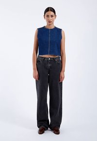 Cropped blue denim vest with raw hem, paired with loose-fitting black jeans, featuring a classic five-pocket design and stitching accents.