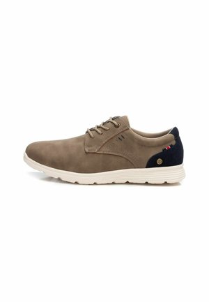 Zapato de ante marrón con un perfil bajo, diseño de cordones, suela de goma blanca y acentos en azul marino en el talón. Presenta detalles de costura mínimos.