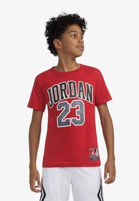 T-shirt in cotone rosso con grandi lettere nere "JORDAN" e il numero "23". Design con scollo tondo classico, maniche corte, con un'etichetta con logo sulla parte inferiore.