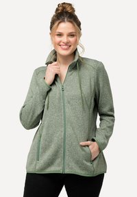 Fleecejacka i strukturerad ljusgrön med hög krage, framfickor med dragkedja och dragsnören. Har två sidofickor och kontrasterande kant.