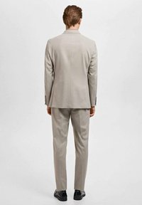 Completo grigio chiaro con giacca strutturata e pantaloni affusolati, realizzato con un tessuto liscio. Completato da scarpe eleganti nere e dettagli di design minimali.