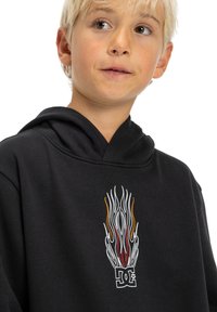 Čierna mikina s kapucňou s dizajnom plameňa v bielej, červenej a oranžovej farbe. Materiál vyzerá jemne, má klokanie vrecko a nastaviteľnú kapucňu.