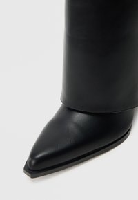Μαύρο δερμάτινο μποτάκι αστραγάλου με μυτερή μύτη, λεία υφή και επικάλυψη στην κορυφή. Ίσια σόλα με μινιμαλιστική άκρη.