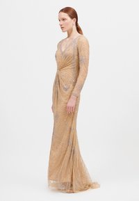 Beige avondjurk met lange mouwen, V-hals en een aansluitende silhouet. Heeft ingewikkelde zilveren kraalwerk en een vloeiende rok.