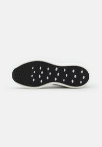 Black rubber shoe sole featuring a textured pattern with raised sections and oval cutouts, surrounded by a white edge for contrast.