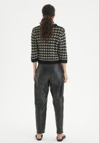 Veste courte à carreaux noir et blanc en tricot texturé, associée à un pantalon en cuir noir taille haute. Sandales noires simples visibles.