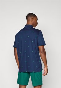 Polo de color navy con patrones de hojas verdes, de manga corta y con cuello. Combinado con pantalones cortos verdes. Tejido suave, corte clásico.