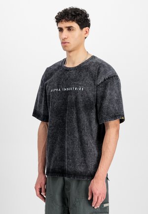 Schwarzes, übergroßes T-Shirt mit strukturierter Oberfläche, auf der Vorderseite mit dem weißen Schriftzug "ALPHA INDUSTRIES". Kurze Ärmel.